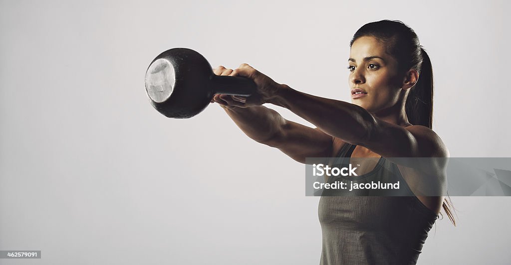 Woman exercise with kettle bell - gym workout Young fitness female exercise with kettle bell. Mixed race woman doing gym workout on grey background Kettlebell Stock Photo