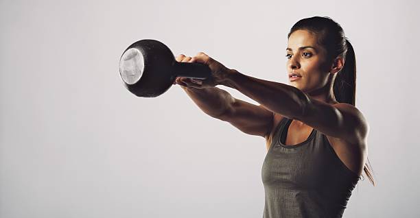 Woman exercise with kettle bell - gym workout Young fitness female exercise with kettle bell. Mixed race woman doing gym workout on grey background kettlebell stock pictures, royalty-free photos & images