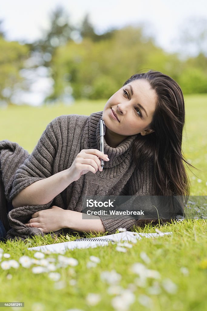 Задумчивый симпатичные брюнетка лежа на траве с ее Блокнот - Стоковые фото 20-29 лет роялти-фри