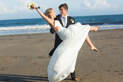 Dynamic young bridegroom lifting his beautiful wife on the beach