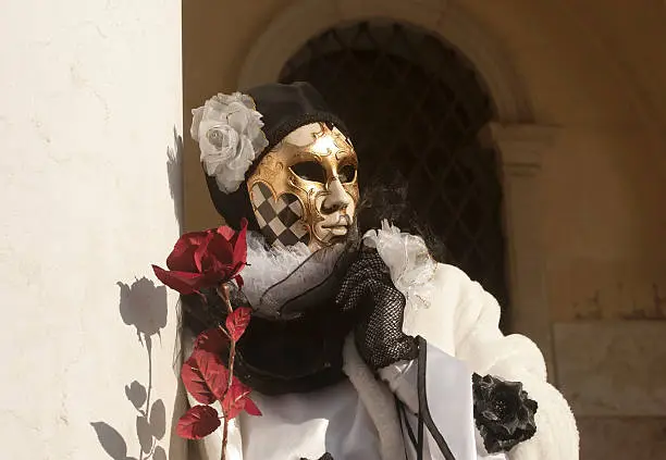 Masked person with traditional "Pierrot" costume posing in front the Doges Palace on Piazza San Marco in Venice, Italy.