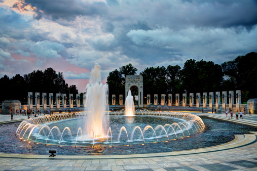 A photograph of the World War II Memorial at sunset. The Memorial is located on the National Mall in Washington, DC and is the first national memorial dedicated to all who served during World War II. It is located on 17th Street, between Constitution and Independence Avenues, and is flanked by the Washington Monument to the east and the Lincoln Memorial to the west. This photo was taken at sunset.