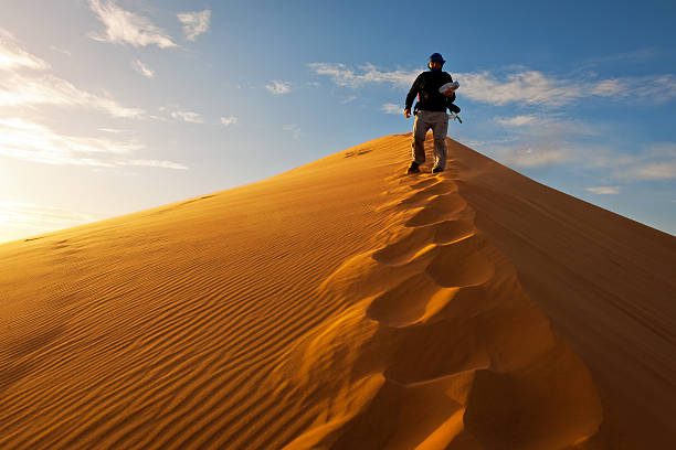 Photographer walking on sand dune in Erg Chebbi desert at sunrise, Morocco, Africa.