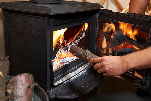 Man Putting Log Onto Wood Burning Stove Traditional method of heating house wood burning stove stock pictures, royalty-free photos & images