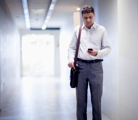 Businessman standing in the corridor and looking down at his phone