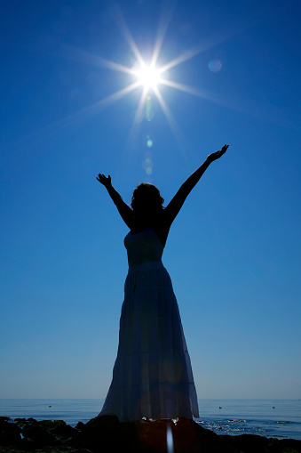Silhouette of a woman with her arms raised to the sun