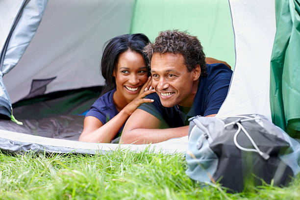 Happy african couple camping outdoors Happy african couple lying together in camping tent looking away smiling women lying down grass wood stock pictures, royalty-free photos & images