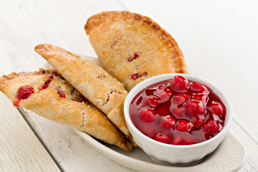 A high angle close up shot of several freshly baked cherry turnovers and a bowl of cherry filling.