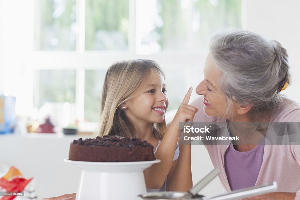 Granny having fun with granddaughter icing a cake - Стоковые фото Бабушка роялти-фри