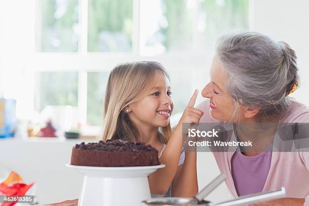 Granny Having Fun With Granddaughter Icing A Cake — стоковые фотографии и другие картинки Бабушка - Бабушка, Торт, Шоколад