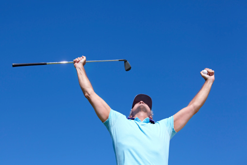 Low-angle shot of a mature male golfer with his arms raised in celebration