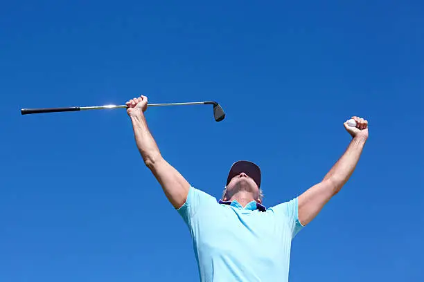 Low-angle shot of a mature male golfer with his arms raised in celebration