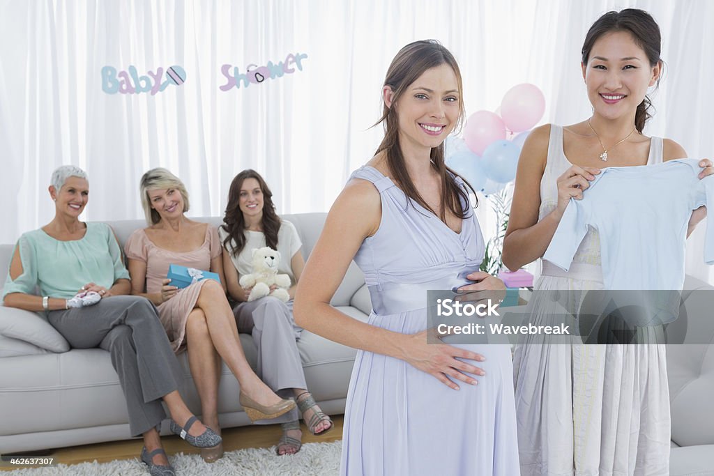 Cheerful expecting woman talking about baby clothes with her fri Cheerful expecting woman talking about baby clothes with her friend while other friends looking at them 20-29 Years Stock Photo