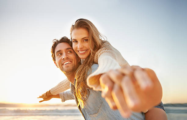 Celebrating their love! A loving young couple standing on the beach with their arms outstretched and holding hands romantic activity stock pictures, royalty-free photos & images