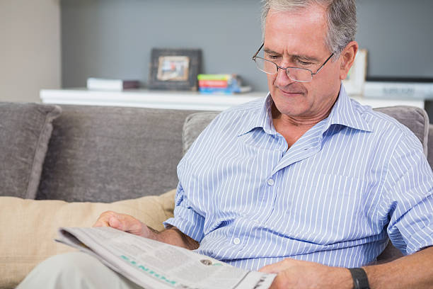 istock Serious mature man reading newspaper on his sofa 462642049