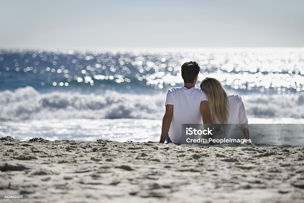 Reflecting on their love A young couple sitting together on the beach and admiring the beautiful view Couple - Relationship Stock Photo