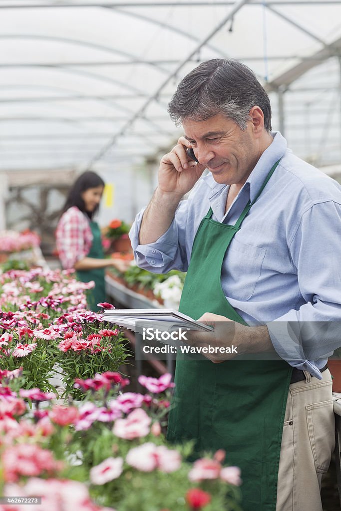 Garden center employee on the phone holding a notepad Garden center employee on the phone holding a notepad while checking the flowers 20-29 Years Stock Photo