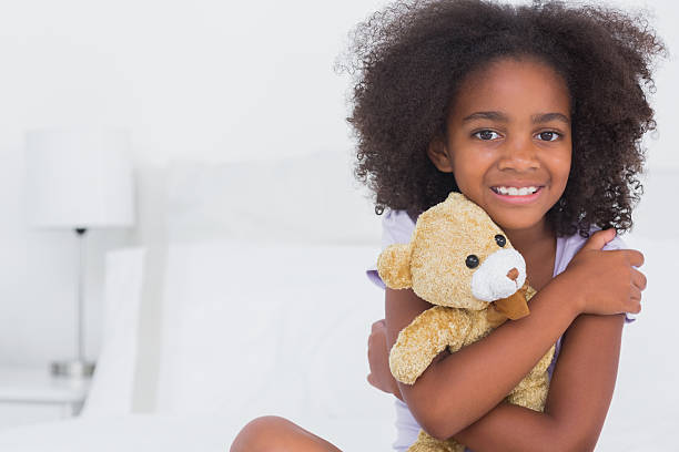 istock Girl sitting on bed smiling at camera holding teddy bear 462672283