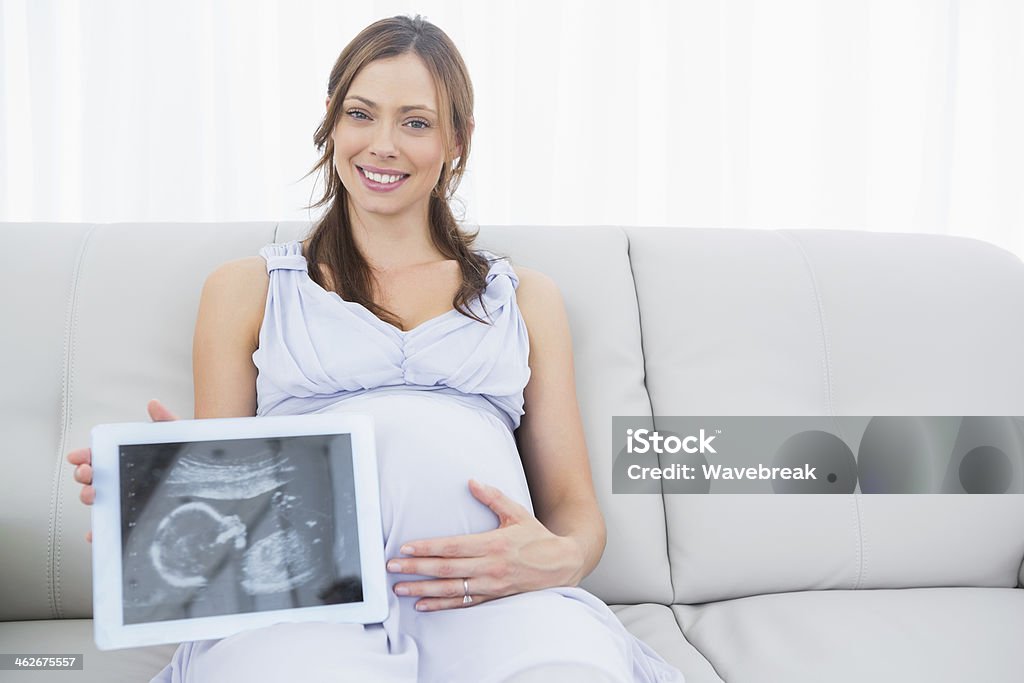Happy pregnant woman holding baby ultrasound scan on tablet pc Happy pregnant woman holding baby ultrasound scan on tablet pc sitting on the couch 30-39 Years Stock Photo