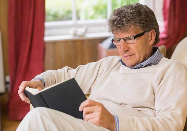 istock Concentrated mature man reading a book sitting on his sofa 462675859