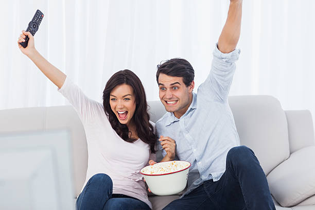 istock Couple raising arms while watching television 462680311