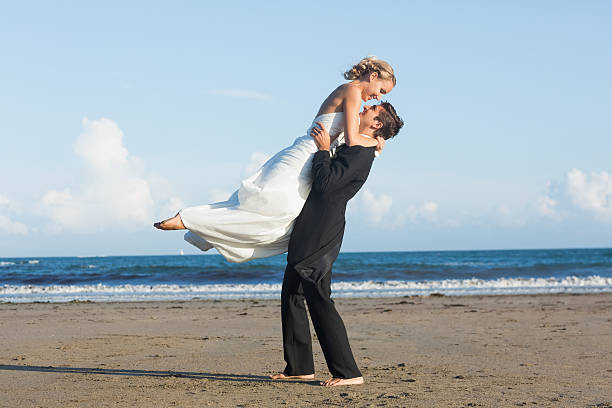 Dynamic young bridegroom lifting his blonde wife on the beach