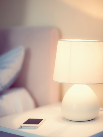 White smartphone lying on a bedside table next to a lamp