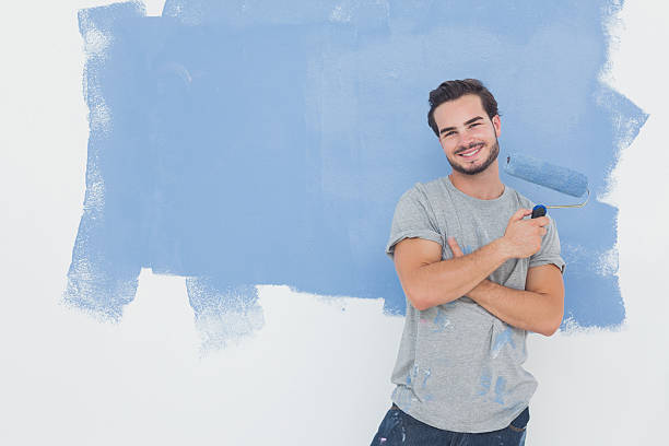 Happy man with paintbrush in front of wall