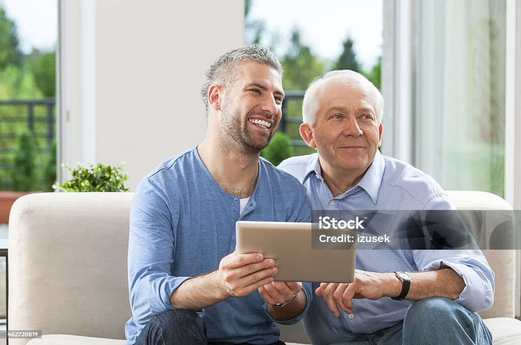 Father and adult son with digital tablet Happy father and adult son sitting on sofa at home and using a digital tablet together. 30-39 Years Stock Photo