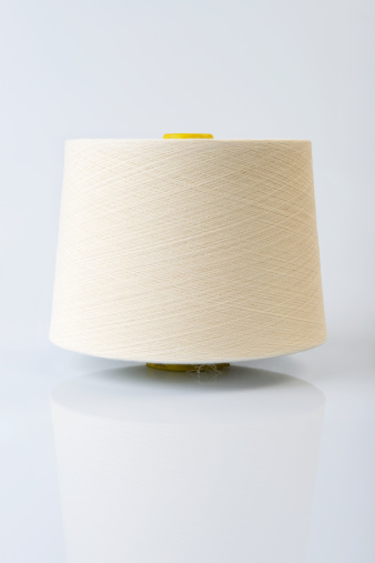 White spool of yarn on white background with its reflection.