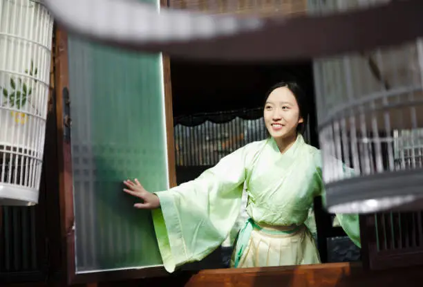 Happy east asian teenage girl dress in Hanfu (traditional Chinese clothing) opening the wooden window.