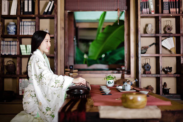 East asian teenage girl dress in Hanfu (traditional Chinese clothing) sitting in the room, playing the zheng.