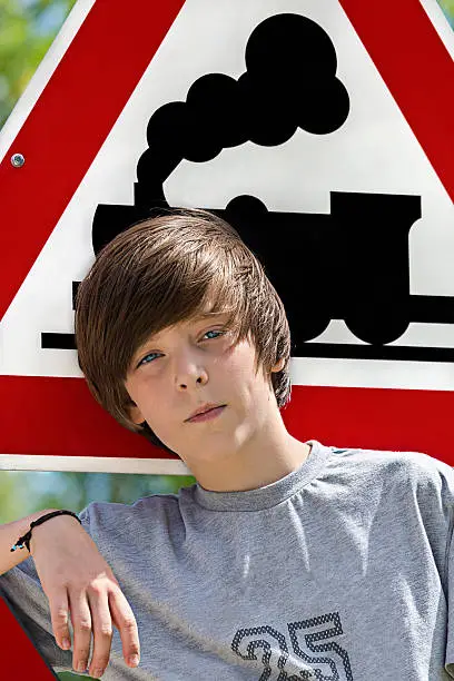 portrait of a cool boy in front of a locomotive traffic sign.