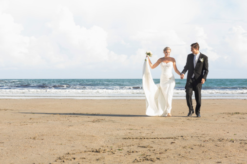 Beautiful lovely young newlyweds walking together on the beach