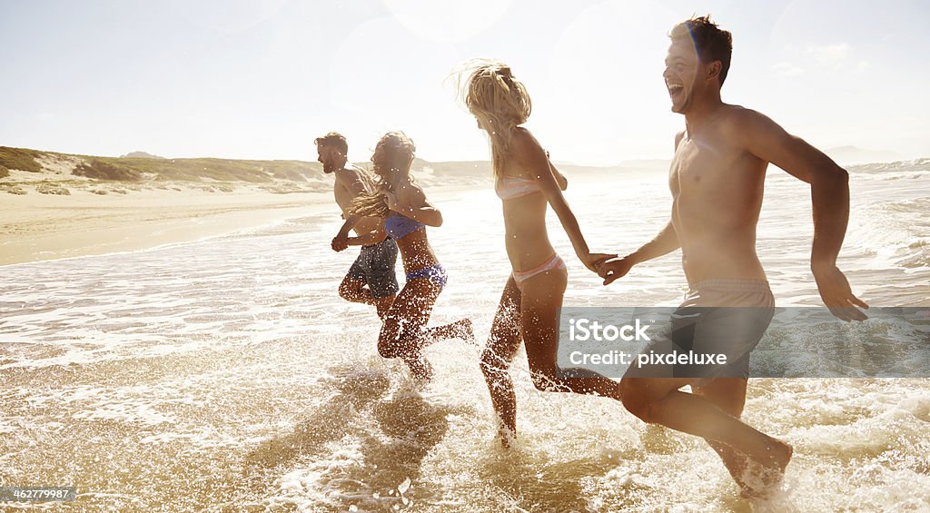 Feeling refreshed and ready for summer! Two young couples running through the water at the beach Adult Stock Photo