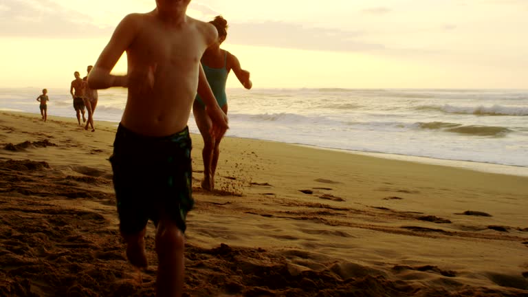 A family together running on the beach on a tropical vacation in a location like Kauai, Maui, Hawaii, Fiji, Tahiti, or the Carribean during an amazing sunset.