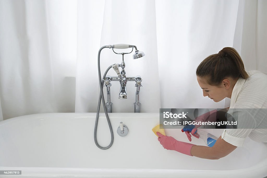 Woman Cleaning Bathtub Young woman cleaning up the bathtub with sponge and cleaner at home Adult Stock Photo