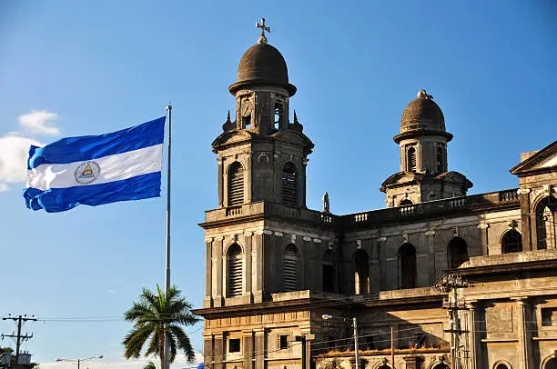 Managua, Nicaragua: bell towers of the Old Cathedral and the giant Nicaraguan flag flying at Plaza de la Revolución / Plaza de la República, built in concrete and steel and designed by the engineer Pablo Dambach, manufactured and shipped from Belgium, but very damaged by the 1972 earthquake - Antigua Catedral de Santiago de Managua - centro histórico - photo by M.Torres