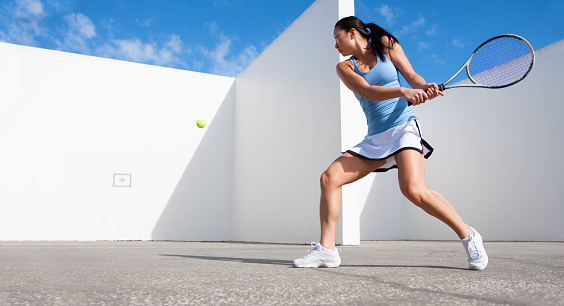 Young female tennis player hitting tennis ball against a wall.  