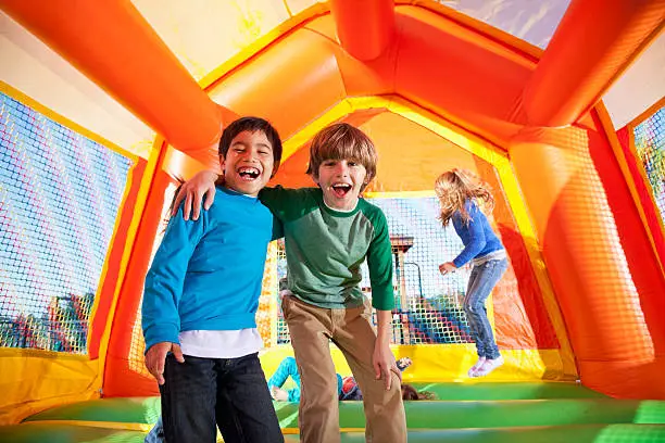 Multi-ethnic boys laughing in bouncy castle, girls jumping in background.