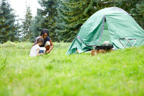 Young mother with her little girl setting up a tent for camping - Outdoors in countryside