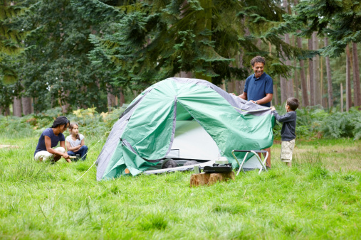 Mixed race family setting up a tent for camping - Outdoors in countryside