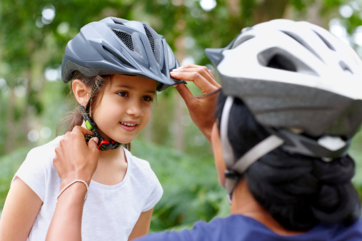 Woman adjusting helmet of a little girl smiling - Outdoors