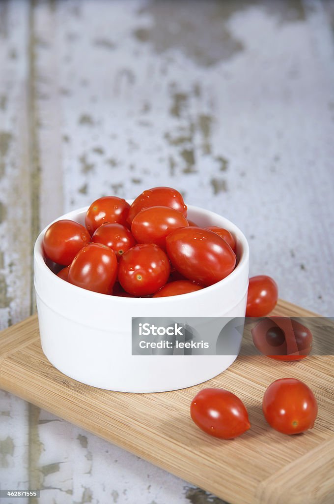 Fresh cherry tomatoes in white bowl Fresh cherry tomatoes in white bowl on wooden cutting board. Shallow depth of field, copy space. Antioxidant Stock Photo