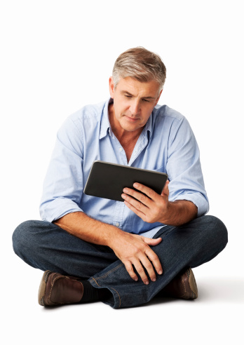 Full length of mature man using digital tablet while sitting on floor against white background. Vertical shot.