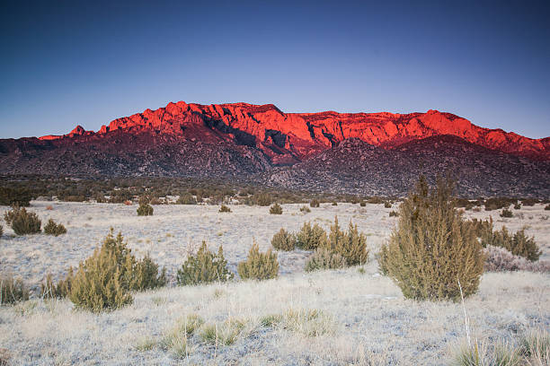 intense mountain landscape sunset deep red alpenglow shines on the desert mountain ridges of peaks with a desert meadow of juniper stands far below.  such beautiful nature scenery can be found in the sandia mountains of albuquerque, new mexico.  horizontal wide angle composition. bernalillo county stock pictures, royalty-free photos & images