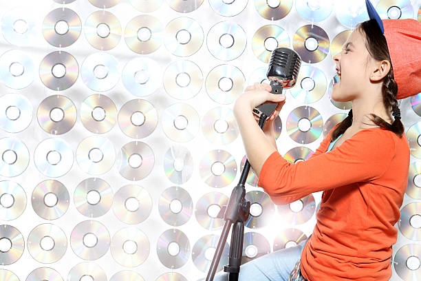 The girl singing karaoke wearing a baseball cap and orange shirt against the wall cd