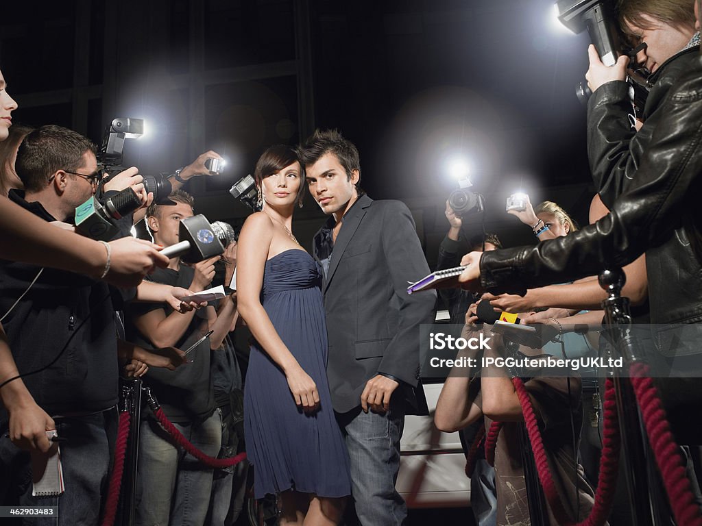 Couple Posing In Front Of Paparazzi Young couple posing on red carpet being photographed by paparazzi Red Carpet Event Stock Photo
