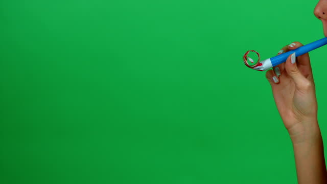 Female blowing colorful party horn on green screen