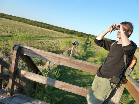 Young man looking off through a binoculars in Biebrza National Park, Poland.